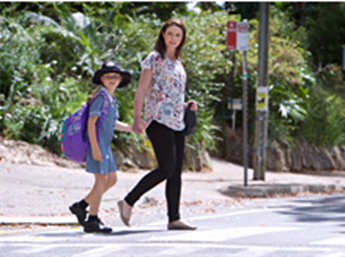 Woman and school kid crossing the road holding hands